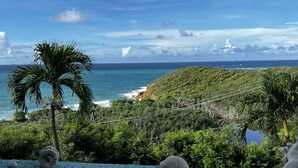 A round table with a white cup and a glass container with seashells, overlooking a coastal landscape with palm trees and a view of the ocean. - ✩ Amazing ocean view (St Thomas)