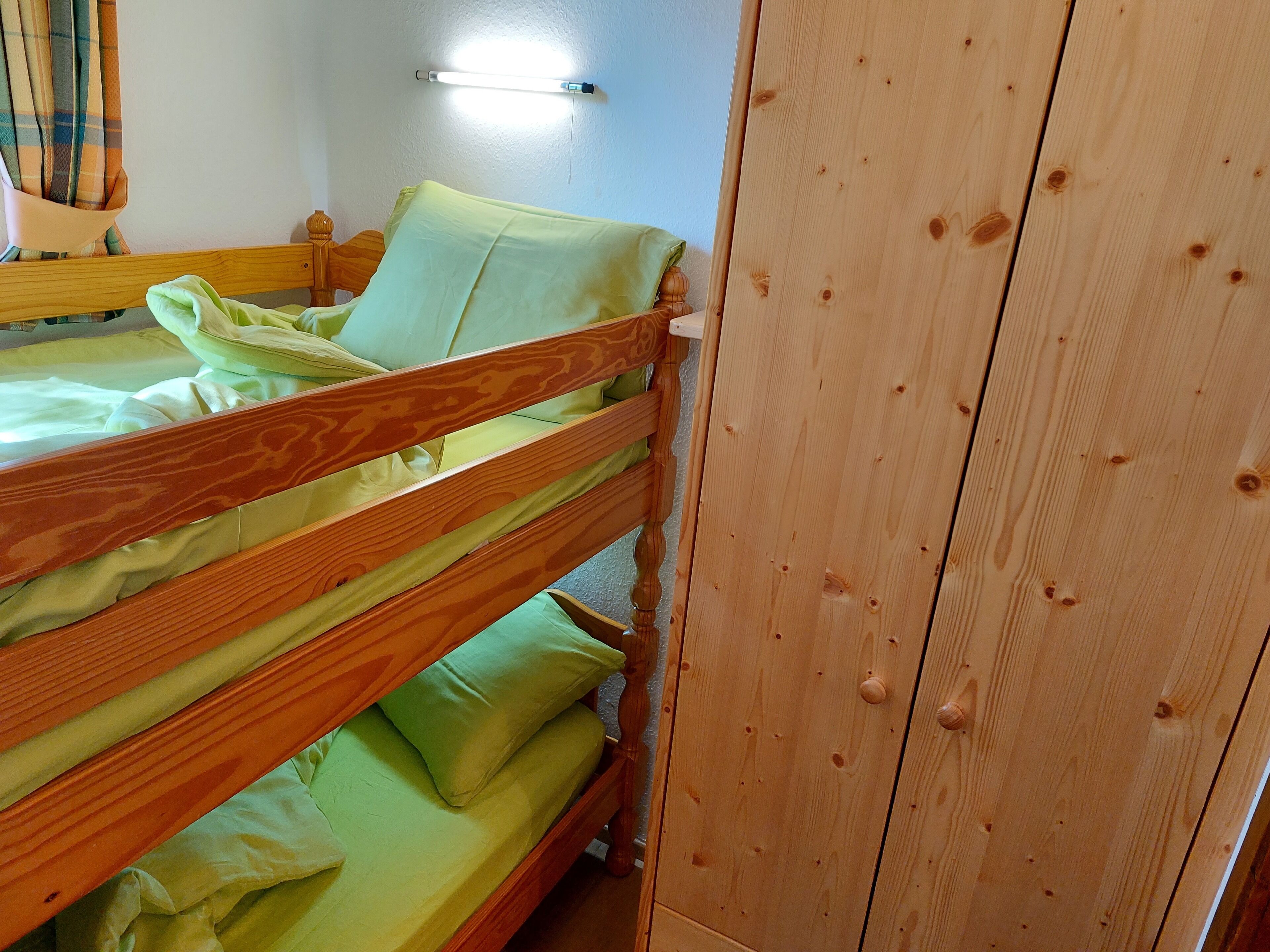 A bunk bed with green bedding in a room with wooden walls and a light fixture on the wall.