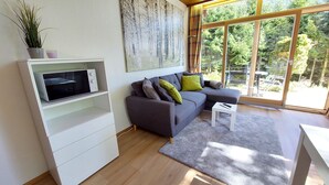 Ein modernes Wohnzimmer mit einer grauen Eckcouch, einer weißen Unterhaltungseinheit und einem großen Fenster mit Blick auf ein bewaldetes Gebiet.