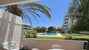 Une terrasse avec une table ronde et des chaises, une piscine et des bâtiments en arrière-plan.