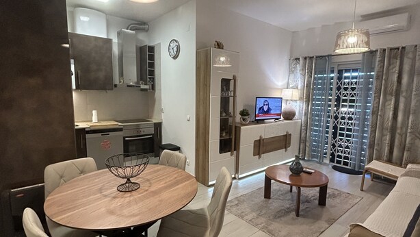 Un salon moderne comprenant un coin repas, une cuisine et un téléviseur en arrière-plan.