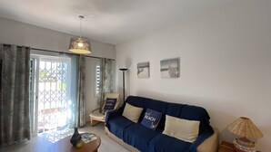 Un salon avec un canapé, une table, une lampe et une vue sur l’extérieur, visible à travers une porte vitrée.