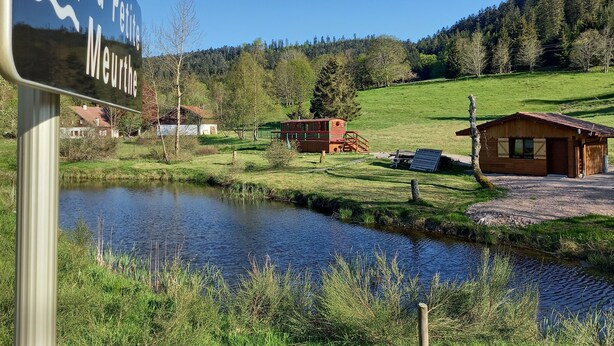 A rural landscape with a sign reading "La Petite Meurthe," a small house, and a pond.