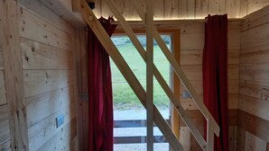 A wooden cabin room with a large window, red curtains, and a wooden ceiling beam.