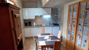A compact kitchen with white cabinets, a dining table with chairs, and a refrigerator.
