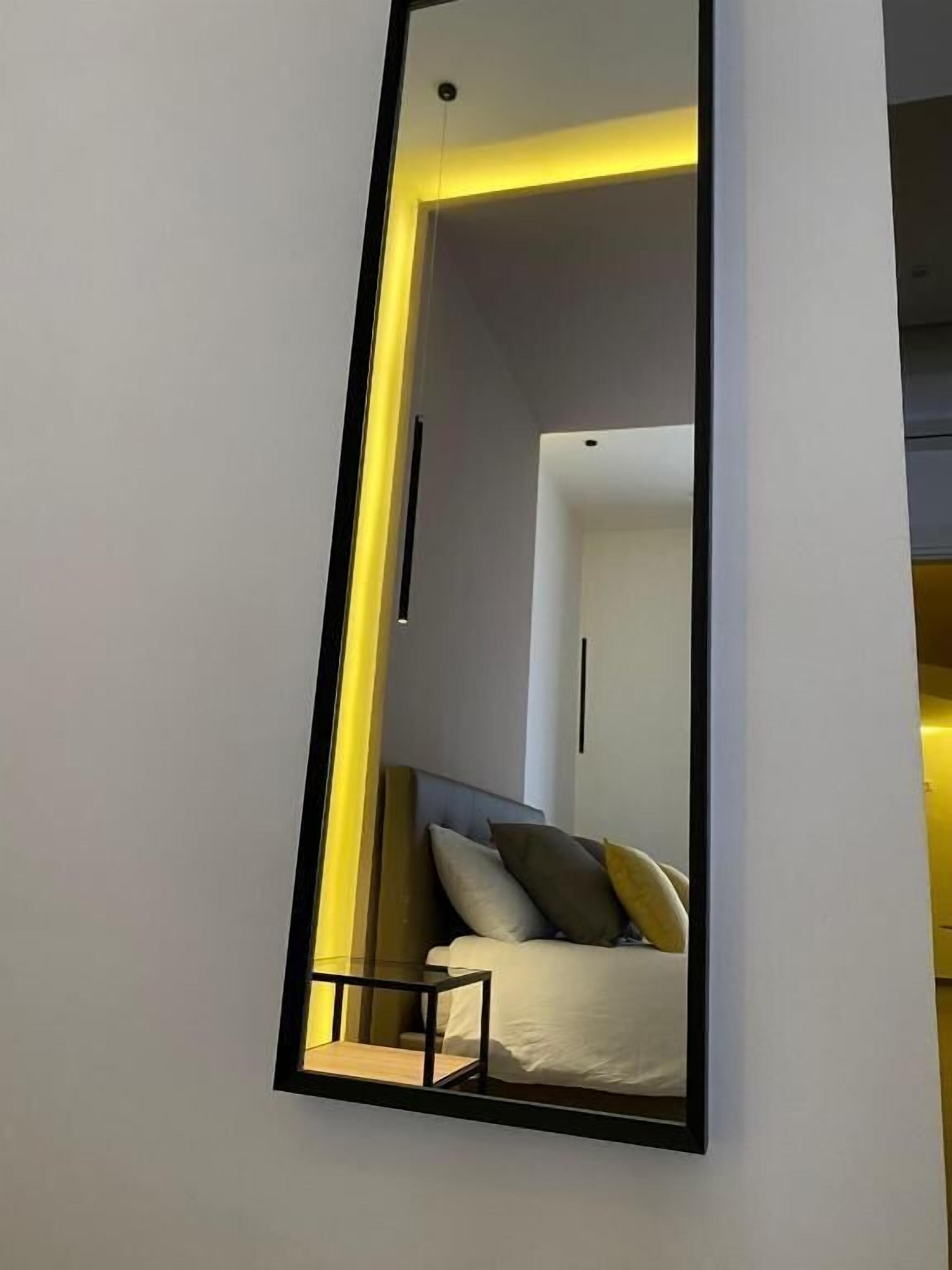 A modern bedroom with a large mirror, a bed with pillows, and a bedside table.