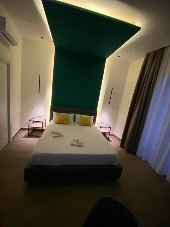 Une chambre d’hôtel moderne avec un grand lit, deux tables de chevet et un plafond au design original, de couleur verte.