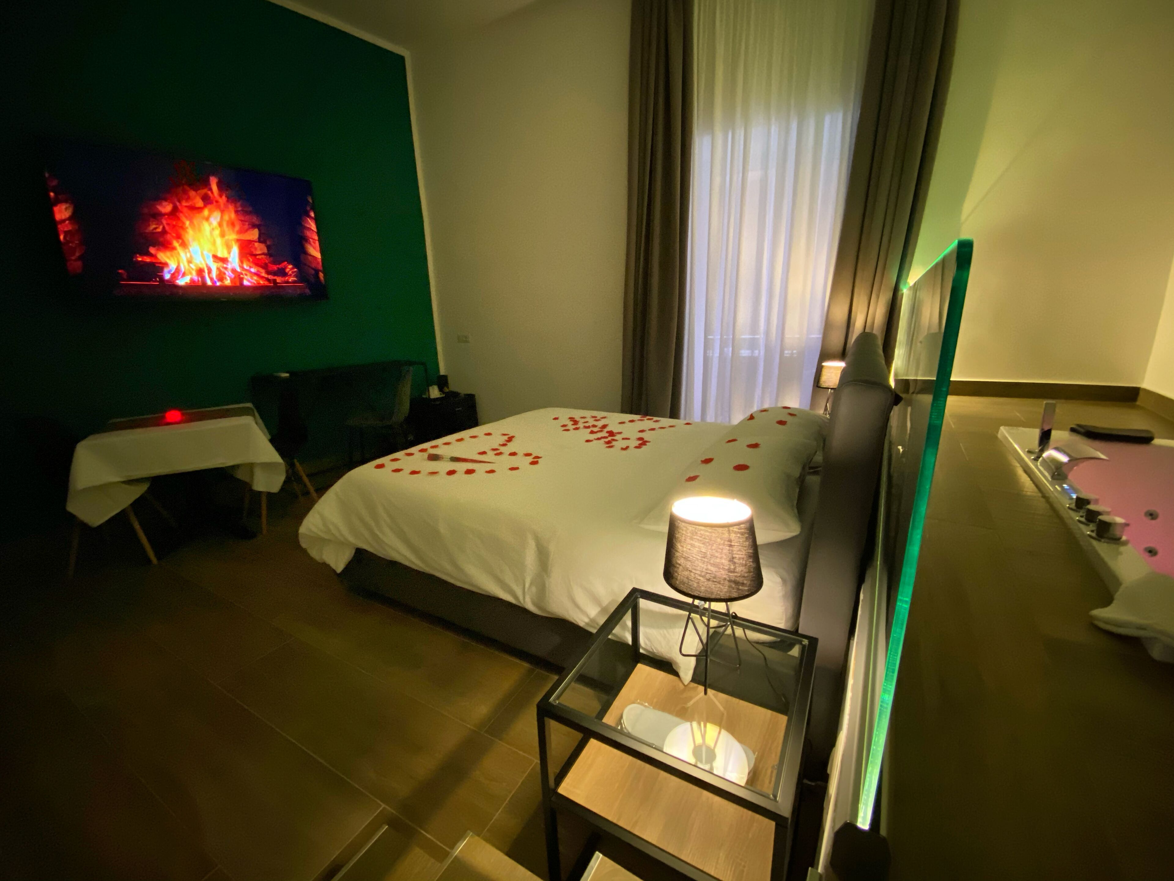 A hotel room with a bed, a TV mounted on the wall, a bedside table with a lamp, and a small table with a chair.