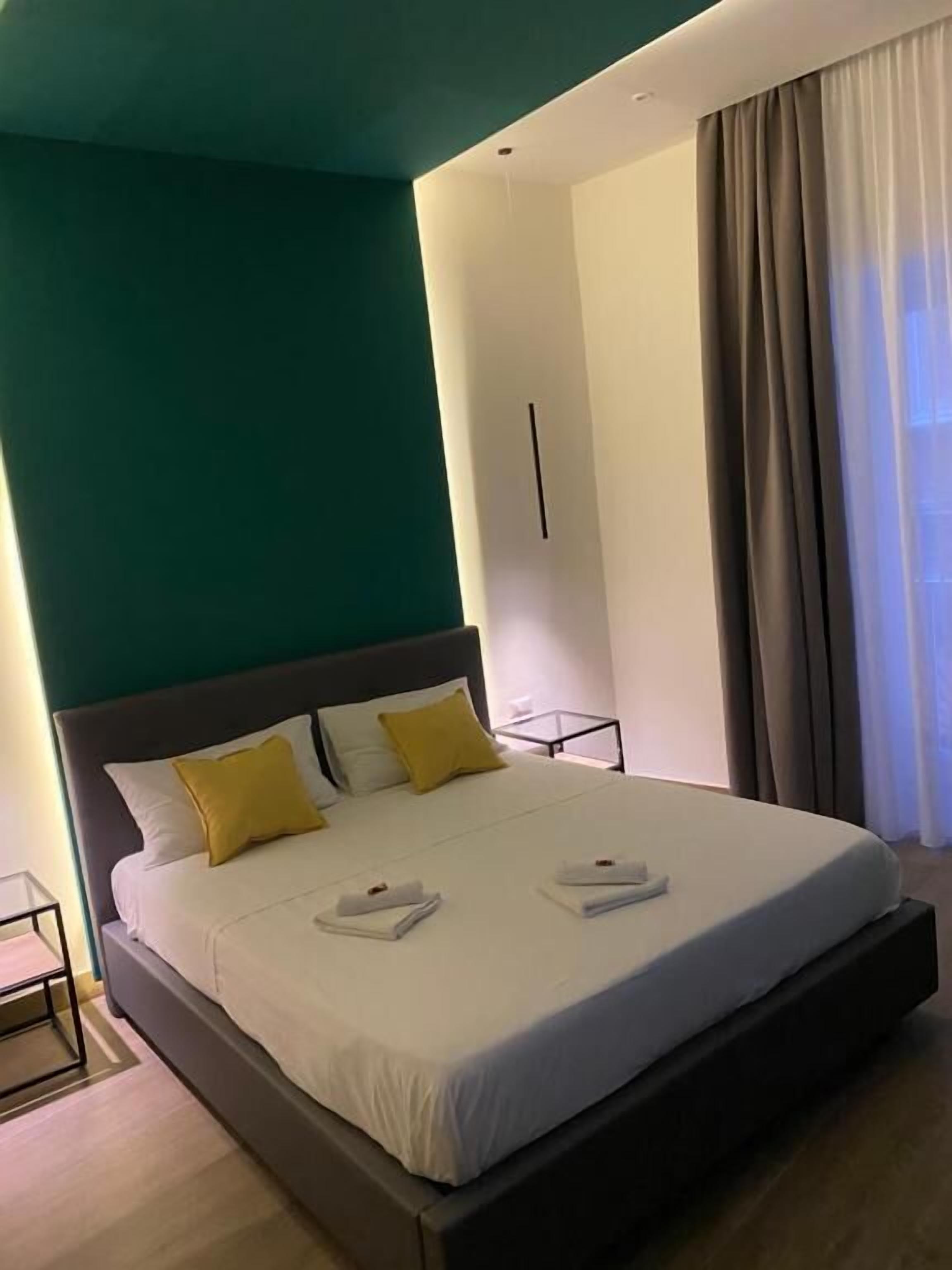 A modern hotel room with a large bed, two pillows, a nightstand, and a window with curtains.