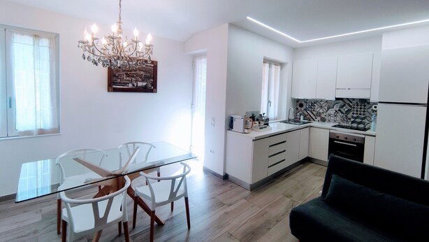 Una cocina moderna con armarios blancos, una estufa negra y un comedor con mesa de vidrio y sillas blancas.