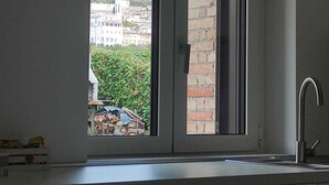 Una cocina con ventana, un lavamanos y vistas a edificios y zonas verdes.