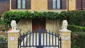 Una casa de dos pisos con fachada de piedra, contraventanas marrones y una entrada porticada con estatuas de leones a cada lado.