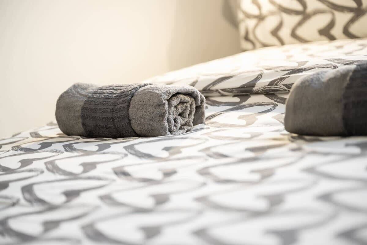 Ein Bett mit einer gemusterten Tagesdecke und zwei aufgerollten Handtüchern.