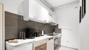 A modern kitchen with white cabinetry, a built-in oven, and a dishwasher. - Apartment close to Theresienwiese (München)