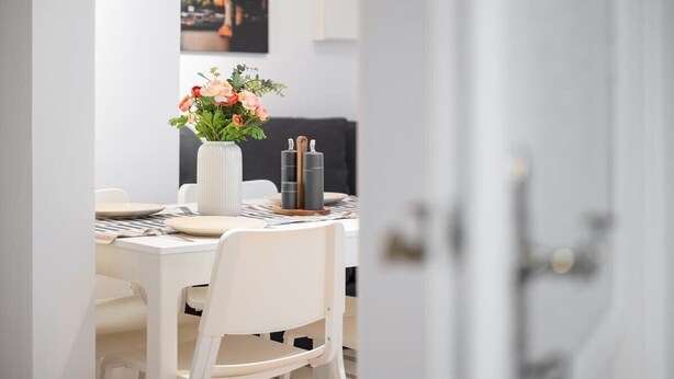 A dining area with a white table set for two, a vase with flowers, and a black and white striped tablecloth. - Apartment close to Theresienwiese (München)