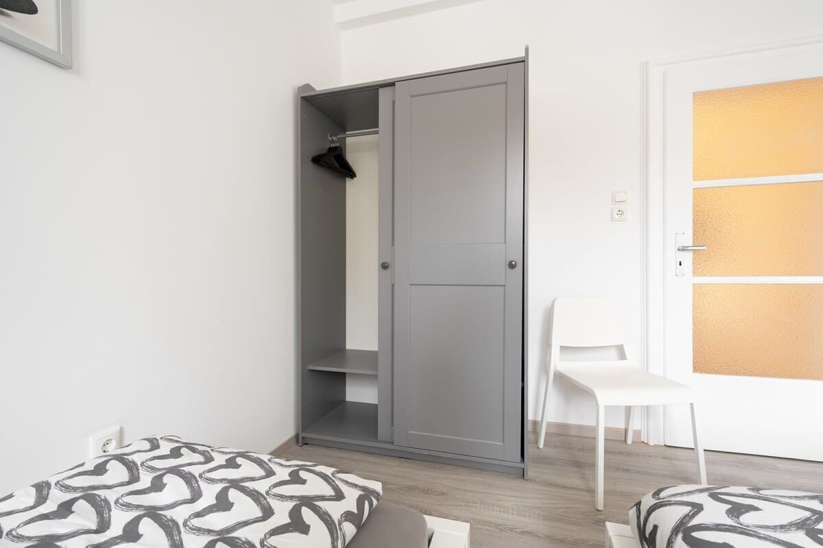 A bedroom with a grey wardrobe, a white chair, and patterned bedding.