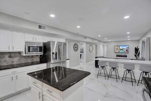 Una cocina moderna con armarios blancos, encimera de granito, electrodomésticos de acero inoxidable y una barra con taburetes.