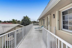 A balcony with a metal railing, a lounge chair, and a window with blinds.