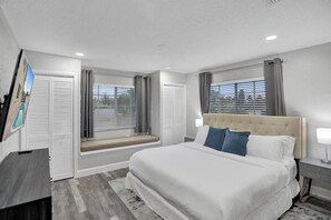 A bedroom with a large bed, bedside tables, a window with blinds, and a view of the outside.