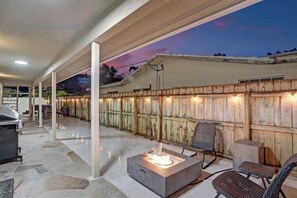 An outdoor patio area with a fire pit, seating, and a wooden fence. - Incredible 7BR | Game Room Heated Pool and Jacuzzi (Deerfield Beach)