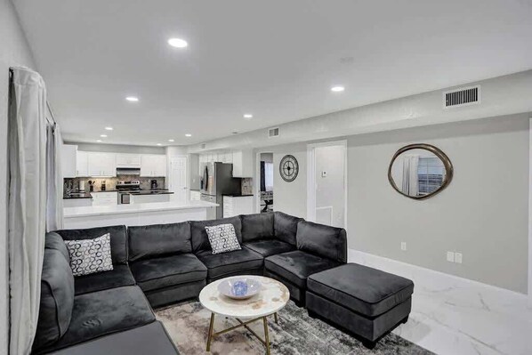 A modern living room with a sectional sofa, a coffee table, and a kitchen in the background.