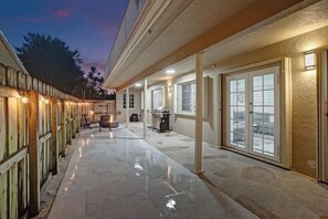 A covered outdoor patio with a stone floor, a grill, and a seating area.