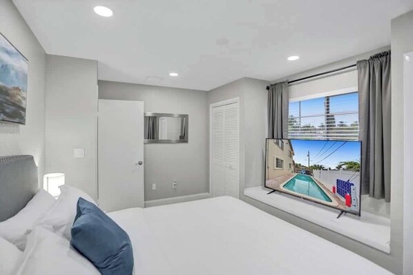 Habitación de hotel con cama, ventana con vista a una piscina, puerta y televisor montado en la pared.
