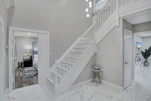 A staircase with white railings leading to a second floor, a small round table with a lamp, and a view of a bedroom with a bed and nightstand.