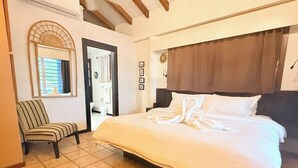 Een slaapkamer met een groot bed, een stoel, een spiegel en een deur naar een andere kamer.