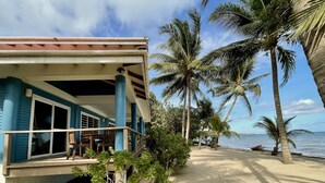 Een pand aan het strand met een overdekte veranda, palmbomen en een zandstrand.