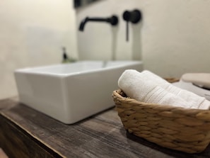 A bathroom sink with a white basin, a wooden basket with a white towel, and a faucet with a black handle.