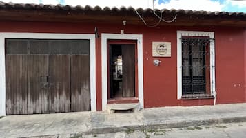 Un edificio rojo con puerta de madera, una reja metálica y una ventana con barrotes decorativos.