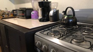 A kitchen with a gas stove, a kettle, a coffee maker, and various kitchen appliances on the counter. - Casa Cheleb (San Cristóbal de las Casas)
