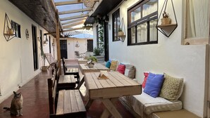 A covered outdoor seating area with wooden tables and benches, a sofa with cushions, and hanging planters. - Casa Cheleb (San Cristóbal de las Casas)