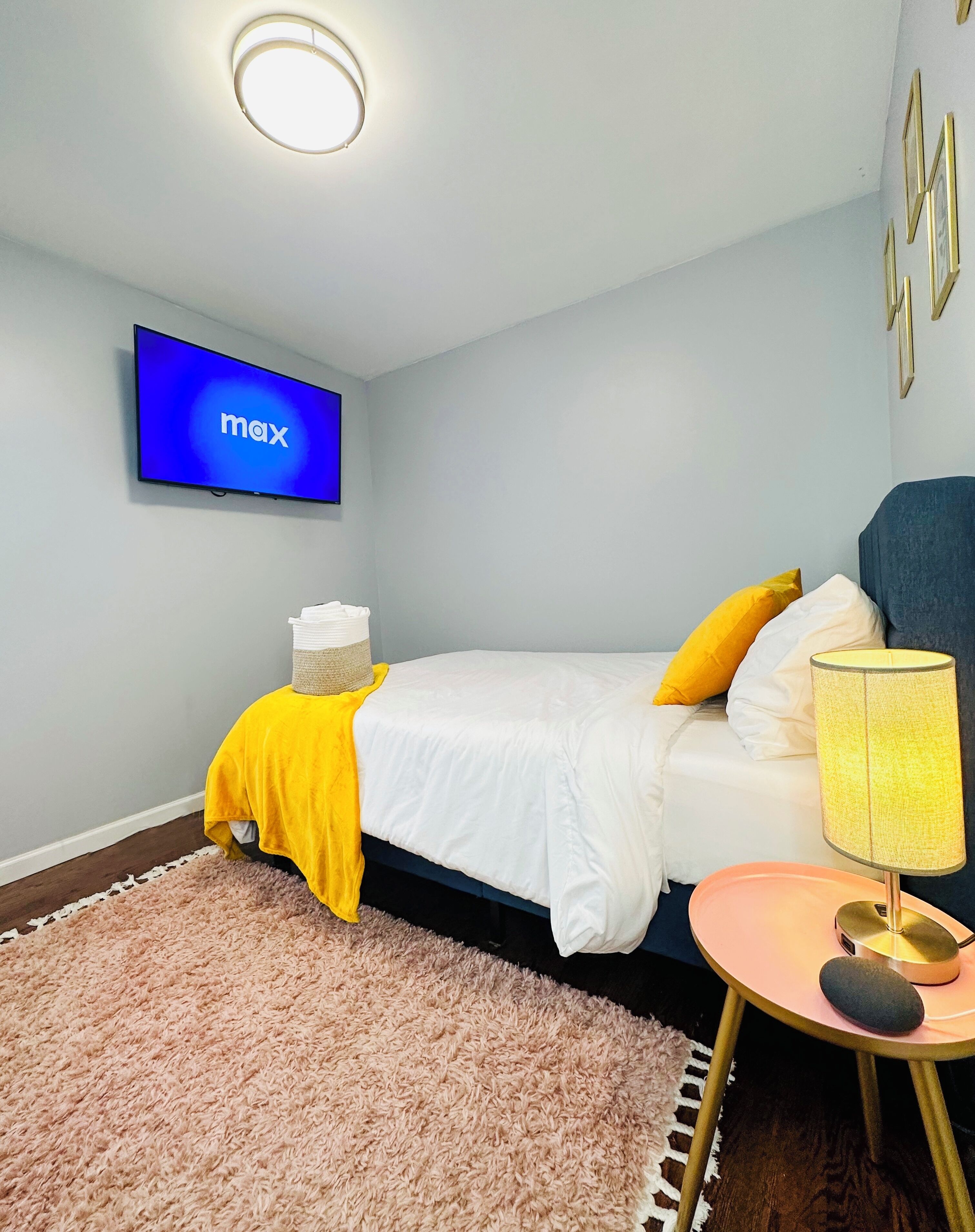 A modern bedroom with a bed, a TV mounted on the wall, a bedside lamp, and a small round table.