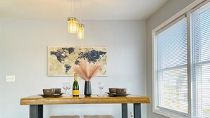 A dining area with a wooden table, two barstools, a world map artwork, a vase with pampas grass, and a bottle of champagne. - Modern 3BR 2BA• 5 Min to EWR • 30 Min to NYC  (Elizabeth)