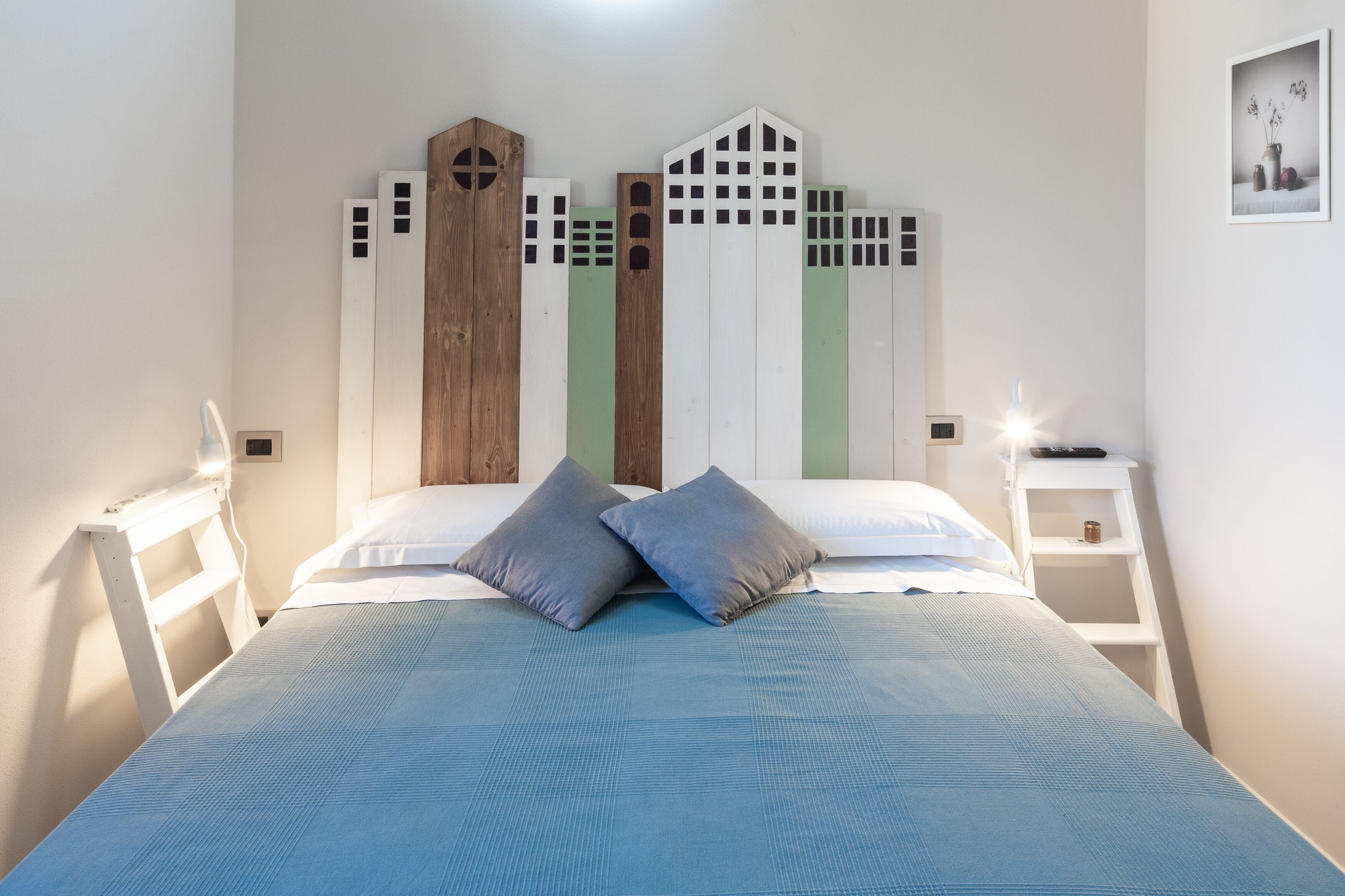 A bedroom with a bed, two bedside tables, and a wall-mounted shelf.