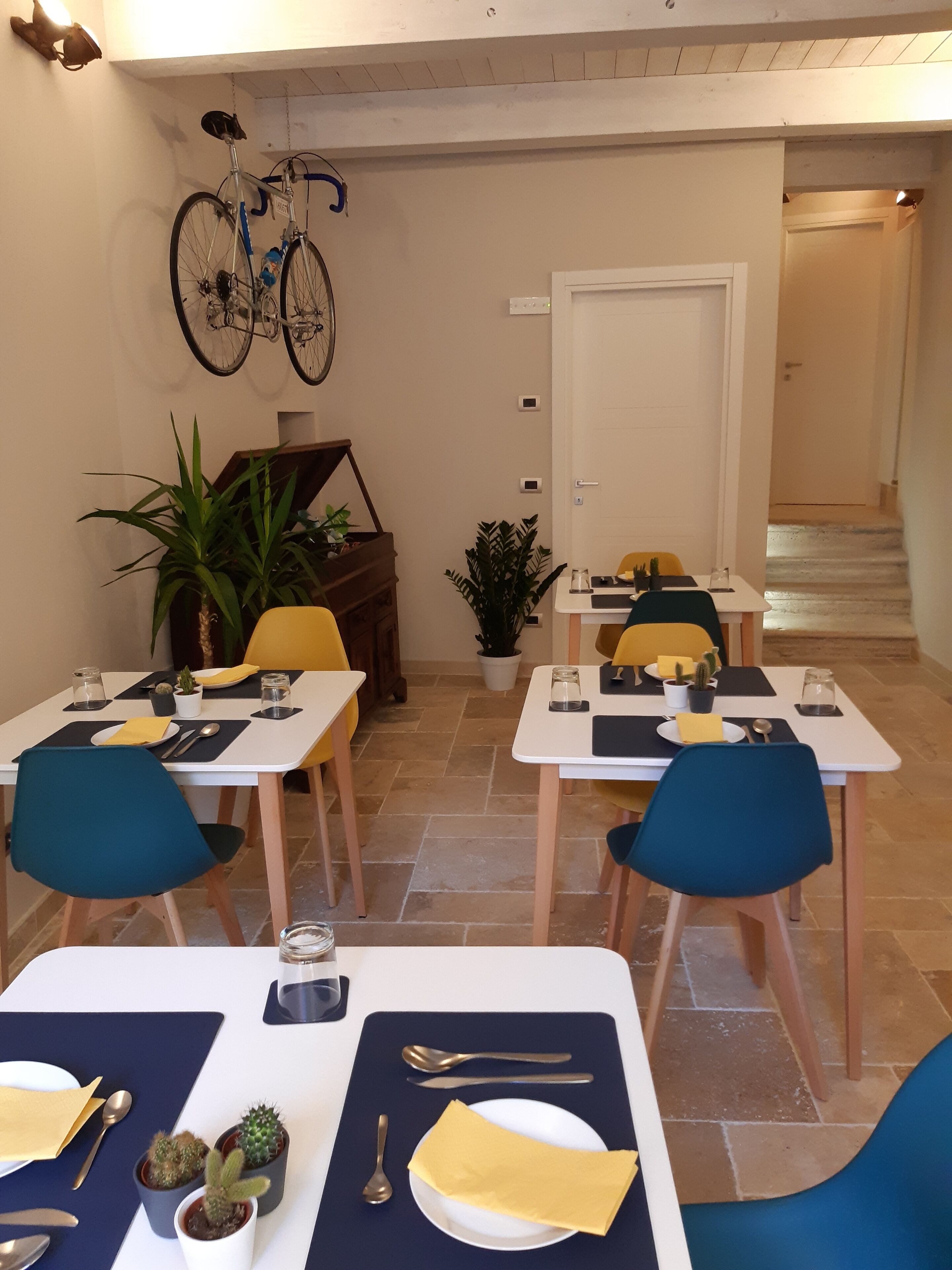 A dining area with tables set for two, chairs, and potted plants.