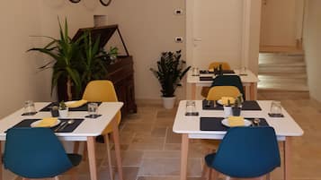 A dining area with tables set for two, chairs, and potted plants.