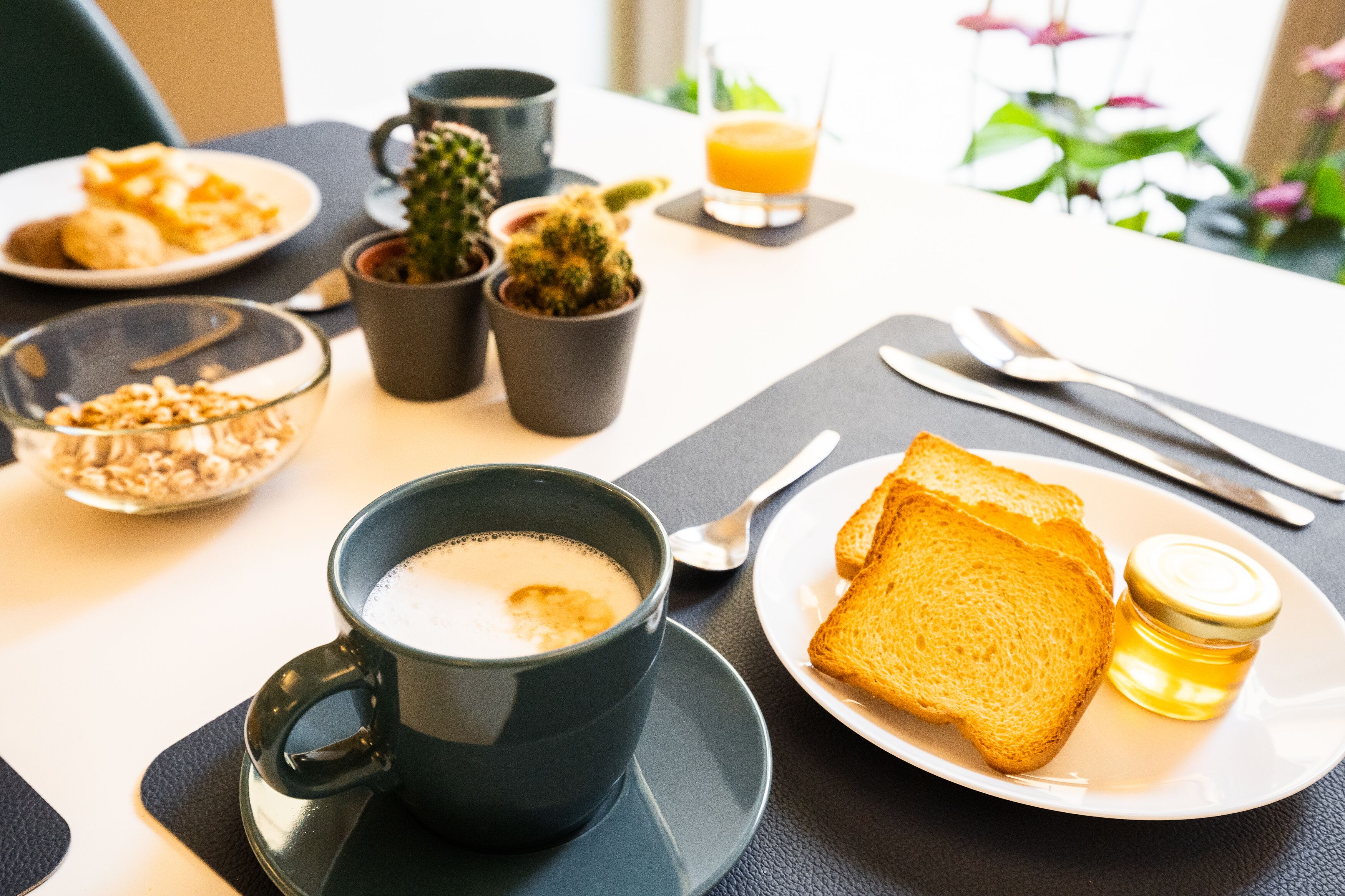 A breakfast table with a cup of coffee, toast, a small jar of honey, and a glass of orange juice.