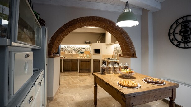 Una cocina con un arco de ladrillo, una mesa de madera con tartas y un reloj en la pared.