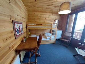 Quarto de cabana de madeira com beliches, mesa de jantar, cadeiras, abajur e janela.