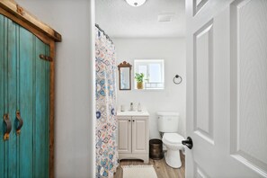 A bathroom with a turquoise door, a patterned shower curtain, a white sink, a toilet, and a mirror above the sink. - Adobe Casa 5min from Downtown SF (Santa Fe)