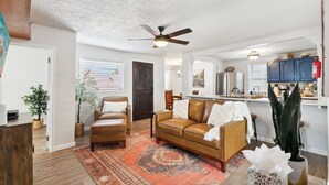 Un salon spacieux avec un canapé en cuir marron, un tapis à motifs et un ventilateur de plafond.