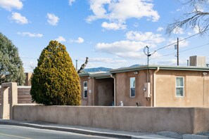 A building with a beige exterior, a small window, and a visible utility box. - Adobe Casa 5min from Downtown SF (Santa Fe)