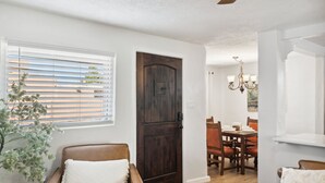 Un salon avec un canapé en cuir marron, une porte en bois et un coin repas comprenant des chaises et une table en bois.