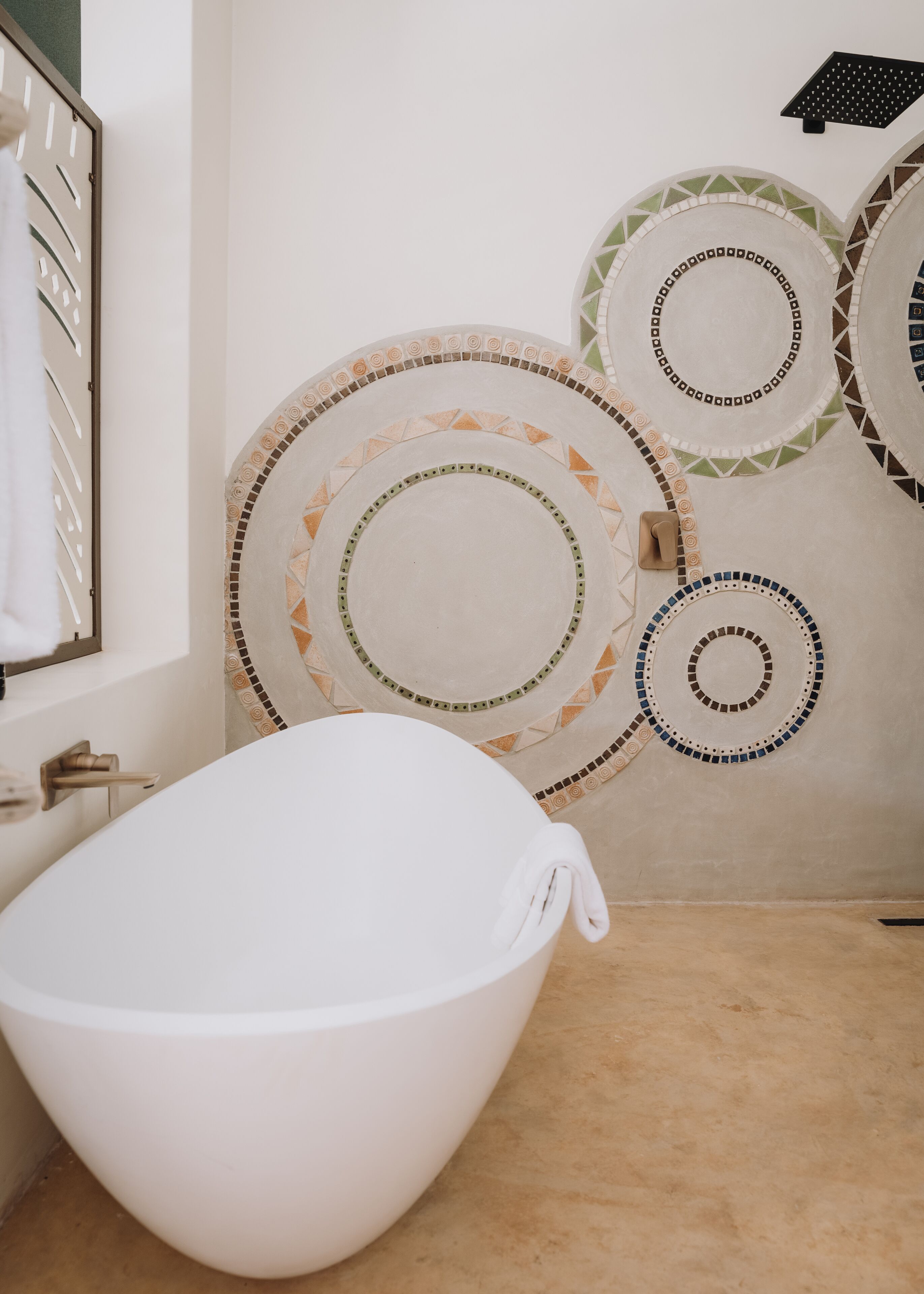 A bathroom with a freestanding bathtub, a mirror, and decorative circular wall tiles.
