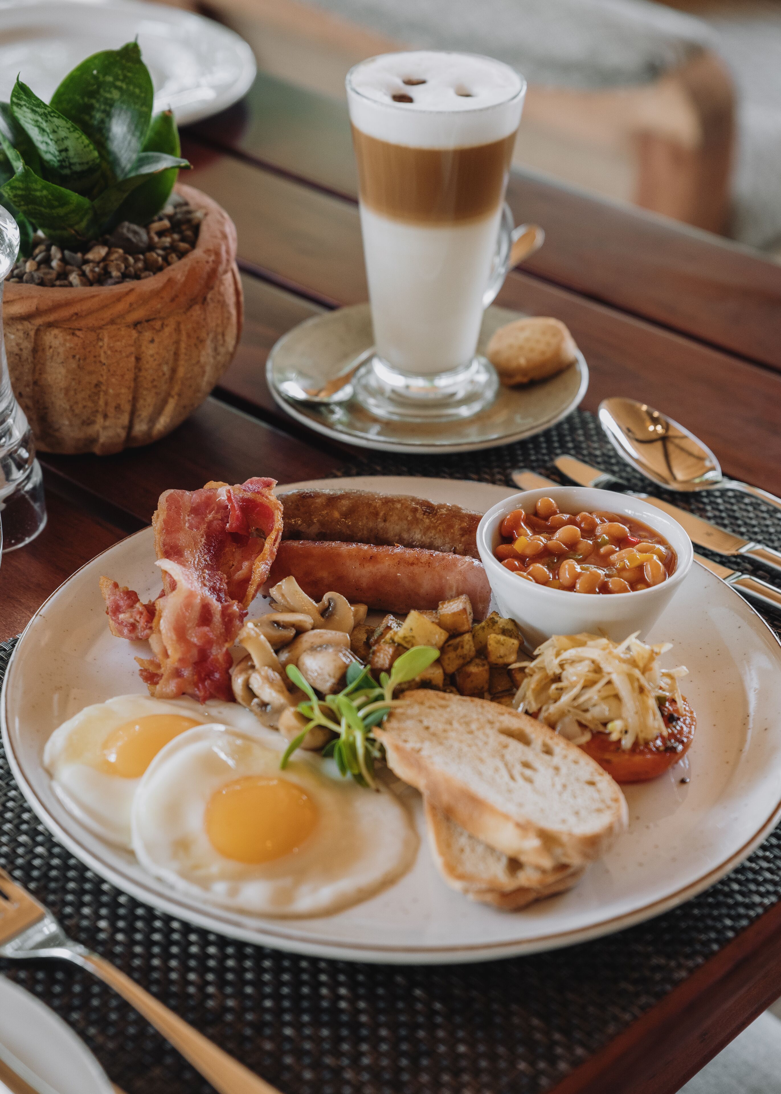 A breakfast plate with eggs, bacon, sausages, beans, mushrooms, and toast.