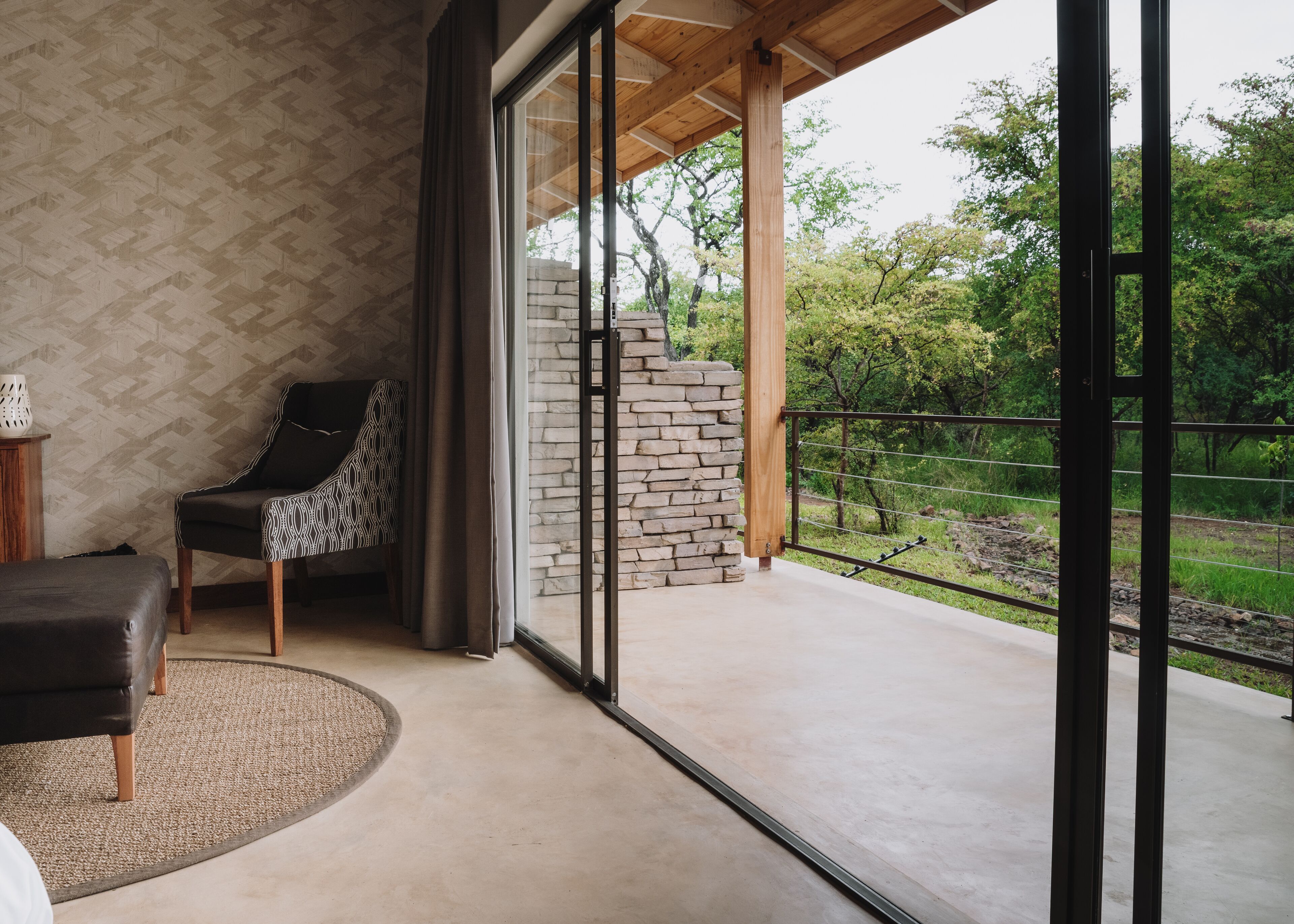 A modern room with a large sliding glass door leading to a balcony, a patterned wall, a black chair, and a stone wall.