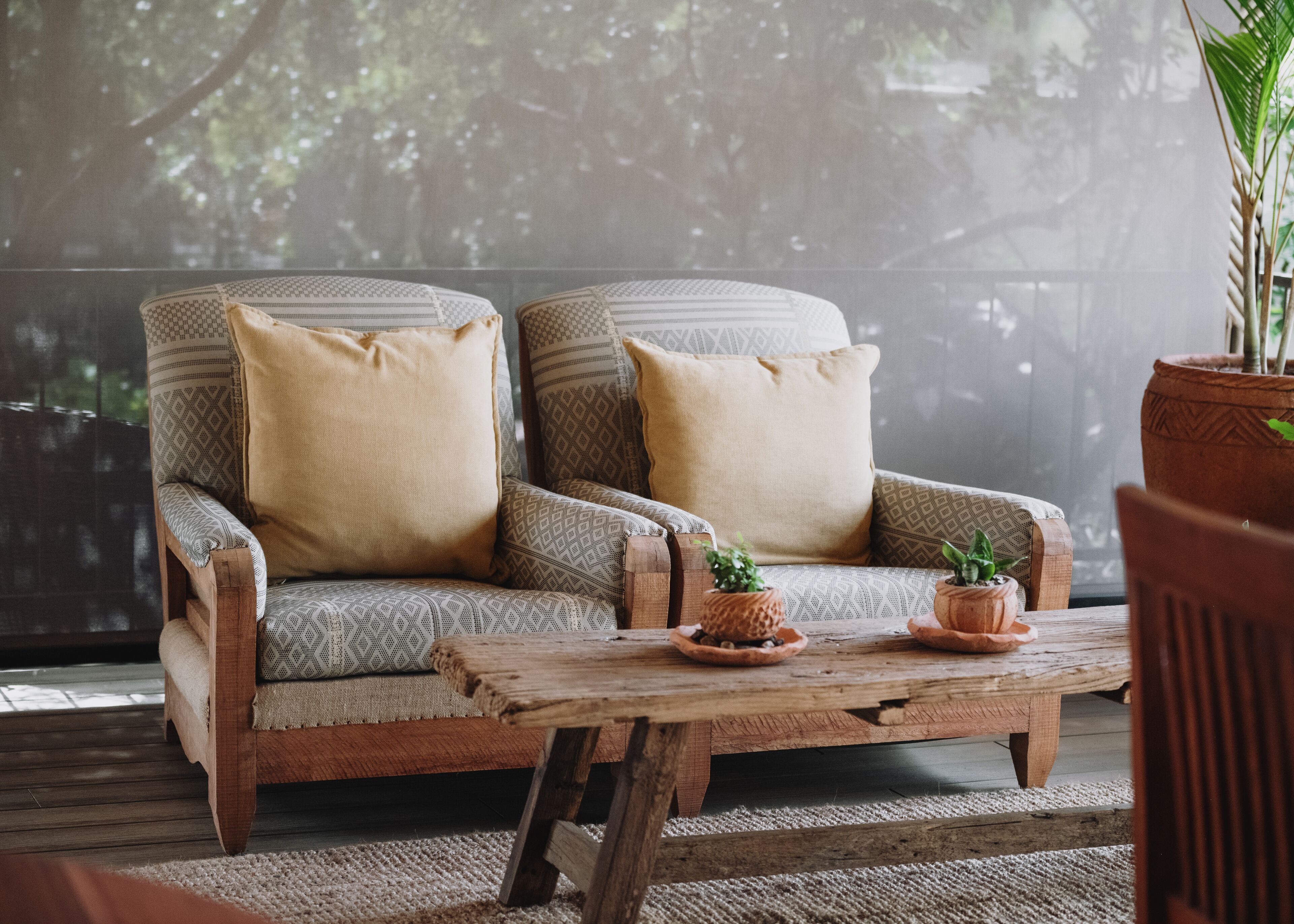 A cozy seating area with two upholstered chairs and a wooden coffee table, featuring potted plants and a rustic design.